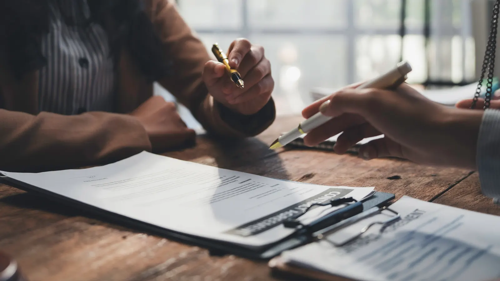 Two professionals reviewing and signing real estate contract documents at a desk, symbolising AML/CTF compliance for real estate agents.